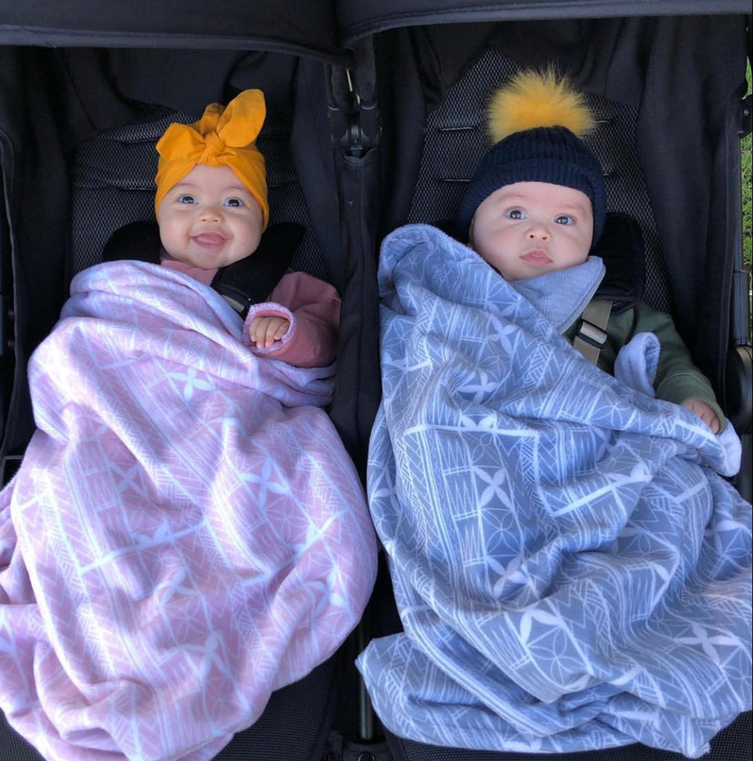 Twin babies in a double pram wrapped in pink and grey-blue Polynesian-inspired minky baby blankets