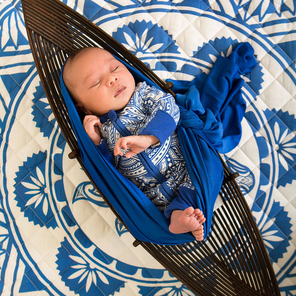 Newborn baby resting in a woven bassinet over a Royal Blue Pacific-inspired baby playmat