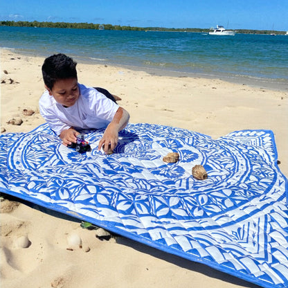 Boy playing on a blue and white Polynesian-inspired baby playmat on the beach